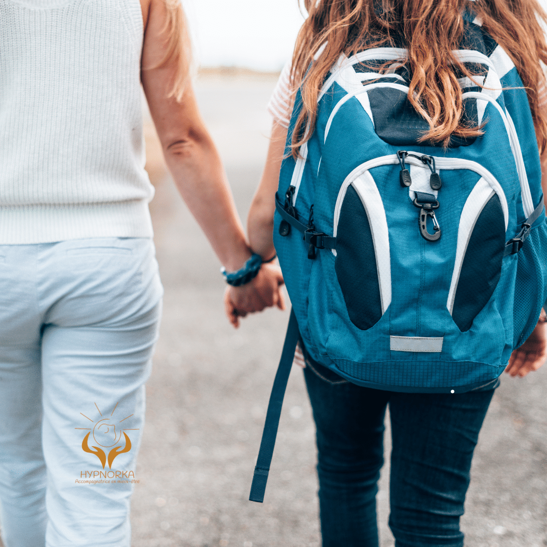 Jeune avec un sac à dos turquoise tenant la main d’un parent sur un chemin.